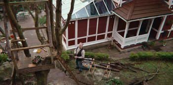 Movie still from “Sex Education” (2019), created by Laurie Nunn – A man standing next to a tree in a yard; Wide shot, Low angle