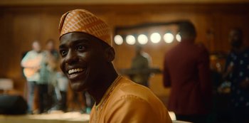 Movie still from “Sex Education” (2019), created by Laurie Nunn – A man with a turban smiles for the camera; Close Up shot, Over the shoulder angle