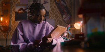 Movie still from “Sex Education” (2019), created by Laurie Nunn – A young girl sitting at a table looking at an ipad; Medium shot, Over the shoulder angle
