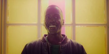 Movie still from “Sex Education” (2019), created by Laurie Nunn – A young man smiles brightly in front of a window; Close Up shot, Low angle