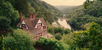 Movie still from “Sex Education” (2019), created by Laurie Nunn – A red and white house sitting on top of a hill next to a river; Extreme Wide shot, High angle