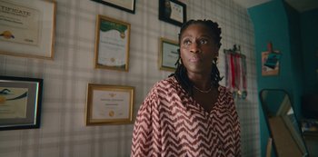 Movie still from “Sex Education” (2019), created by Laurie Nunn – A woman standing in front of a wall with many framed certificates; Medium shot, Low angle