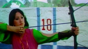 Movie still from “Shirkers” (2018), directed by Sandi Tan – A woman is holding a bow and aiming at a target; Medium shot, Low angle