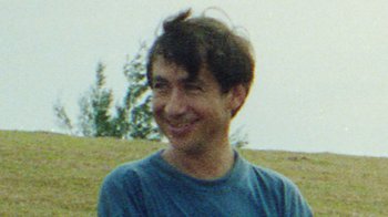 Movie still from “Shirkers” (2018), directed by Sandi Tan – A man smiling for the camera in a grassy field; Close Up shot, High angle