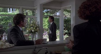 Movie still from “Sleepless in Seattle” (1993), directed by Nora Ephron – A man in a suit is drinking coffee in a kitchen; Wide shot, Over the shoulder angle