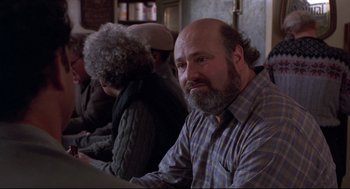 Movie still from “Sleepless in Seattle” (1993), directed by Nora Ephron – A man with a beard sitting next to two other people; Close Up shot, Over the shoulder angle