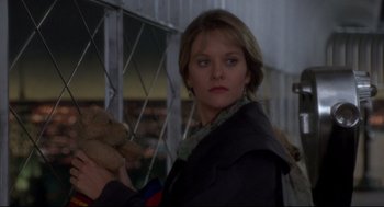 Movie still from “Sleepless in Seattle” (1993), directed by Nora Ephron – A woman holding a teddy bear while standing in front of a fence; Close Up shot, Low angle