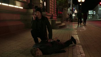 Movie still from “Sniper: Rogue Mission” (2022), directed by Oliver Thompson – A man on a cell phone next to another man on the ground; Wide shot, High angle