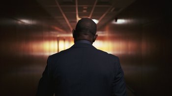 Movie still from “Sniper: Rogue Mission” (2022), directed by Oliver Thompson – A man in a suit is standing in a hallway; Medium shot, Low angle
