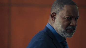 Movie still from “Sniper: Rogue Mission” (2022), directed by Oliver Thompson – A person wearing a suit and tie; Close Up shot, Over the shoulder angle