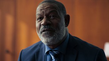 Movie still from “Sniper: Rogue Mission” (2022), directed by Oliver Thompson – An older man wearing a blue suit and a blue tie; Close Up shot, Over the shoulder angle