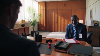 Movie still from “Sniper: Rogue Mission” (2022), directed by Oliver Thompson – A man sitting at a desk in front of another man; Medium shot, Over the shoulder angle
