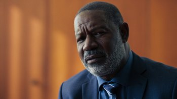 Movie still from “Sniper: Rogue Mission” (2022), directed by Oliver Thompson – An older man wearing a suit and tie; Close Up shot, Over the shoulder angle