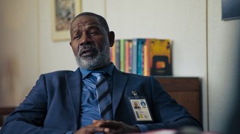 Movie still from “Sniper: Rogue Mission” (2022), directed by Oliver Thompson – An older man wearing a blue suit and tie; Close Up shot, Over the shoulder angle