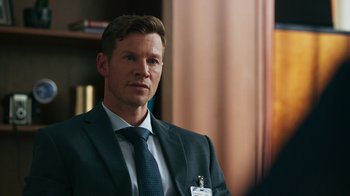 Movie still from “Sniper: Rogue Mission” (2022), directed by Oliver Thompson – A man wearing a suit and tie in a room; Close Up shot, Over the shoulder angle