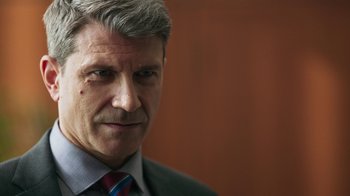 Movie still from “Sniper: Rogue Mission” (2022), directed by Oliver Thompson – A person wearing a suit and tie; Close Up shot, Over the shoulder angle