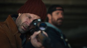 Movie still from “Sniper: Rogue Mission” (2022), directed by Oliver Thompson – A man in a red hat is holding a video camera; Close Up shot, Over the shoulder angle