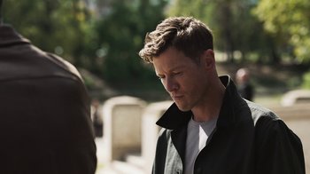 Movie still from “Sniper: Rogue Mission” (2022), directed by Oliver Thompson – A man in a black jacket standing next to a grave; Close Up shot, Over the shoulder angle