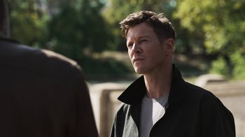 Movie still from “Sniper: Rogue Mission” (2022), directed by Oliver Thompson – A man in a black jacket is standing outside; Close Up shot, Over the shoulder angle