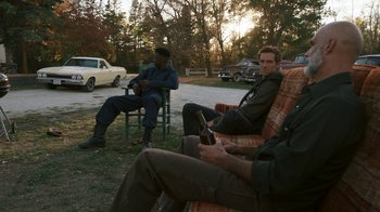 Movie still from “Sniper: Rogue Mission” (2022), directed by Oliver Thompson – A group of men sitting on chairs in a yard; Wide shot, Over the shoulder angle