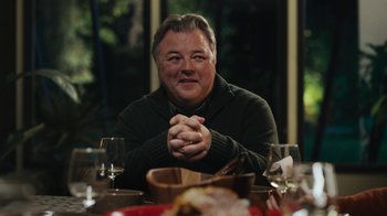 Movie still from “Sniper: Rogue Mission” (2022), directed by Oliver Thompson – A man sitting at a dinner table with his hands clasped; Close Up shot, Over the shoulder angle