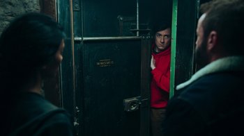 Movie still from “Sniper: Rogue Mission” (2022), directed by Oliver Thompson – A man in a red jacket standing next to a green door; Medium shot, Over the shoulder angle