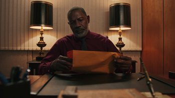 Movie still from “Sniper: Rogue Mission” (2022), directed by Oliver Thompson – An older man sitting at a table looking at an envelope; Close Up shot, Low angle