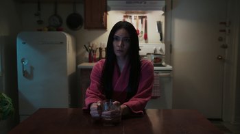 Movie still from “Sniper: Rogue Mission” (2022), directed by Oliver Thompson – A woman sitting at a kitchen table holding a glass; Medium shot, Over the shoulder angle