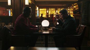 Movie still from “Sniper: Rogue Mission” (2022), directed by Oliver Thompson – Two men sitting at a table with a glass of wine; Medium shot, Over the shoulder angle