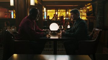 Movie still from “Sniper: Rogue Mission” (2022), directed by Oliver Thompson – Two men sitting at a table in front of a glass of wine; Wide shot, High angle