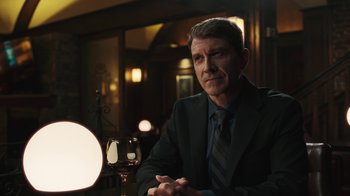 Movie still from “Sniper: Rogue Mission” (2022), directed by Oliver Thompson – A man sitting at a table with a glass of wine; Medium shot, Over the shoulder angle