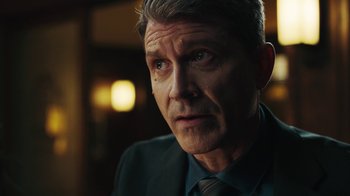 Movie still from “Sniper: Rogue Mission” (2022), directed by Oliver Thompson – A person wearing a suit and tie; Close Up shot, Over the shoulder angle