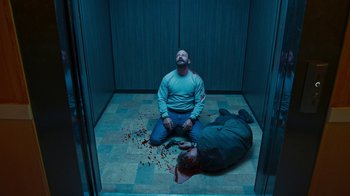 Movie still from “Sniper: Rogue Mission” (2022), directed by Oliver Thompson – A man sitting on the floor next to a dead body; Wide shot, Overhead angle
