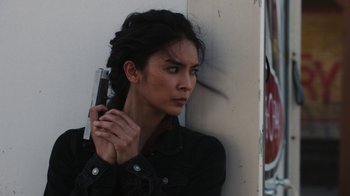 Movie still from “Sniper: Rogue Mission” (2022), directed by Oliver Thompson – A woman holding a gun while standing next to a wall; Close Up shot, Low angle