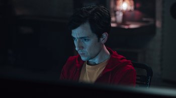 Movie still from “Sniper: Rogue Mission” (2022), directed by Oliver Thompson – A man in a red jacket is sitting in front of a computer; Close Up shot, High angle