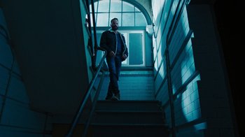 Movie still from “Sniper: Rogue Mission” (2022), directed by Oliver Thompson – A man standing on the stairs of a building; Wide shot, Low angle
