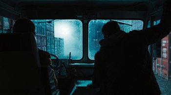 Movie still from “Sniper: Rogue Mission” (2022), directed by Oliver Thompson – A man riding on a bus in the rain; Wide shot, Over the shoulder angle