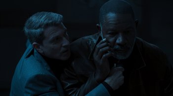 Movie still from “Sniper: Rogue Mission” (2022), directed by Oliver Thompson – A man on a cell phone next to another man; Close Up shot, High angle