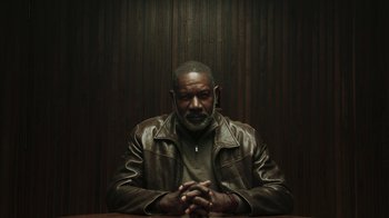 Movie still from “Sniper: Rogue Mission” (2022), directed by Oliver Thompson – A man sitting at a table with his hands crossed; Medium shot, Low angle