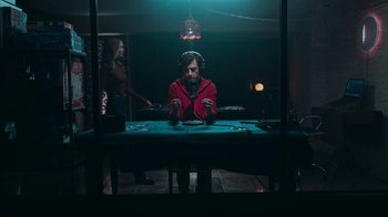 Movie still from “Sniper: Rogue Mission” (2022), directed by Oliver Thompson – A man sitting at a table in a dark room; Medium shot, Low angle