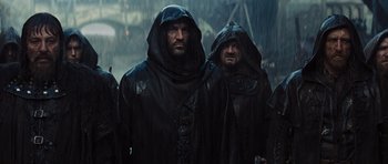 Movie still from “Snow White and the Huntsman” (2012), directed by Rupert Sanders – A group of men in hooded jackets standing in the rain; Medium shot, Over the shoulder angle