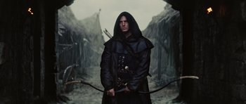 Movie still from “Snow White and the Huntsman” (2012), directed by Rupert Sanders – A man dressed in a black outfit holding a bow and arrow; Medium shot, Low angle