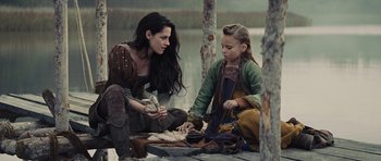Movie still from “Snow White and the Huntsman” (2012), directed by Rupert Sanders – A woman sitting next to a young girl on the shore of a body of water; Medium shot, Over the shoulder angle