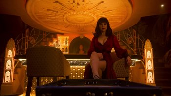 Movie still from “Snowpiercer” (2020), created by Graeme Manson – A woman in a red dress sitting on a chair in front of a bar; Wide shot, Low angle