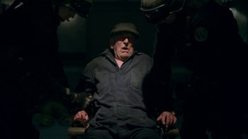 Movie still from “Snowpiercer” (2020), created by Graeme Manson – An old man sitting in a chair with a hat on; Medium shot, High angle