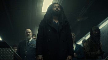 Movie still from “Snowpiercer” (2020), created by Graeme Manson – A man with long dreadlocks standing in front of a group of people; Medium shot, Low angle
