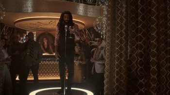 Movie still from “Snowpiercer” (2020), created by Graeme Manson – A man standing in front of a microphone holding a wine glass; Wide shot, Low angle