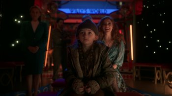 Movie still from “Snowpiercer” (2020), created by Graeme Manson – A young girl sitting next to an older woman in front of a neon sign; Medium shot, Over the shoulder angle