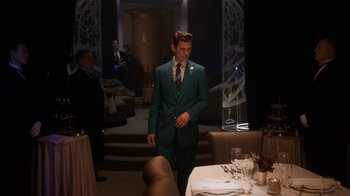 Movie still from “Snowpiercer” (2020), created by Graeme Manson – A man in a green suit standing in front of a table; Medium shot, High angle