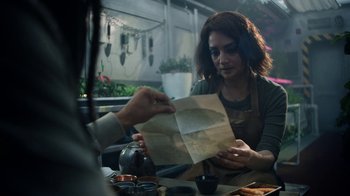 Movie still from “Snowpiercer” (2020), created by Graeme Manson – A woman sitting at a table holding a paper bag; Medium shot, Over the shoulder angle
